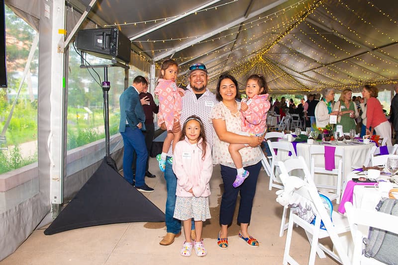 A family of five, two parents and three girls, smiling together in the Stone Soup tent under string lights.